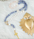 A beaded rosary necklace featuring freshwater pearls, sodalite, and quartz. It has gold-toned metal links, a small gold crucifix, and an Our Lady of Guadalupe centerpiece.